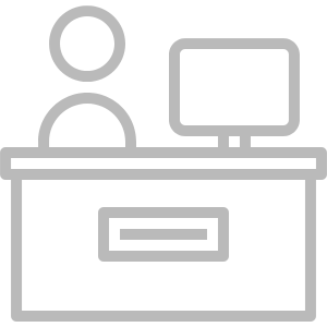 Clerical Staffing: A gray outline of a person seated behind a desk with a computer monitor, symbolizing office work, administration, or a desk job.