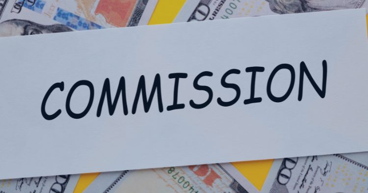 Sales Commission Plans: The word "COMMISSION" written in bold, black letters on a white card, placed over a background of scattered U.S. hundred-dollar bills, symbolizing financial earnings or payments.