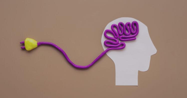 Staffing Mentality: A creative representation of a human head silhouette made from paper, with a purple cable shaped like a brain inside it. The cable's plug, in yellow, extends outwards, symbolizing ideas, connection, or energy.