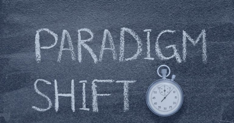 Staffing Paradigm: The words 'PARADIGM SHIFT' are written in white chalk on a blackboard, with a stopwatch placed near the bottom right, symbolizing change and urgency.